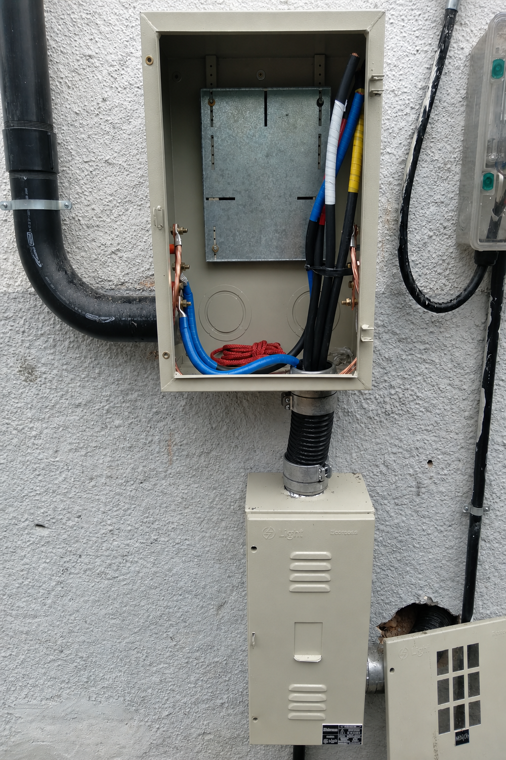 Caixa de medição e entrada de energia em parede externa, com cabos identificados por fitas coloridas