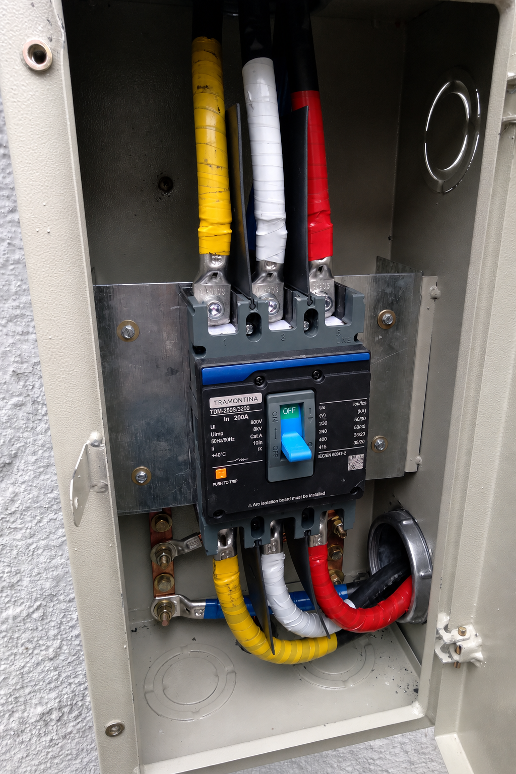 Disjuntor tripolar instalado em quadro metálico, com cabos coloridos conectados
